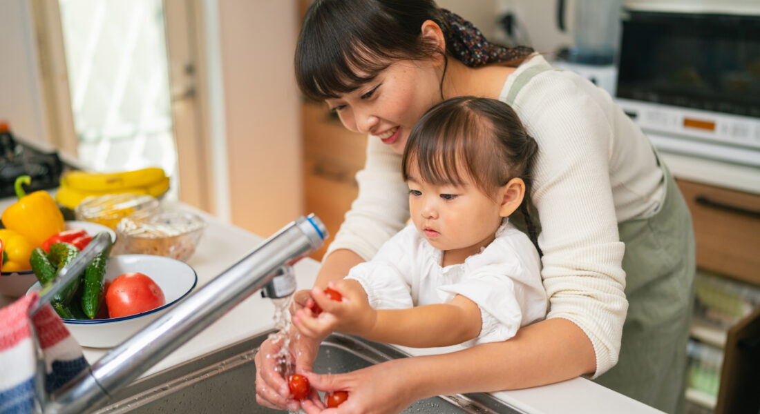 A mother is helping her small daughter washing vegetables and encouraging her for healthy eating.