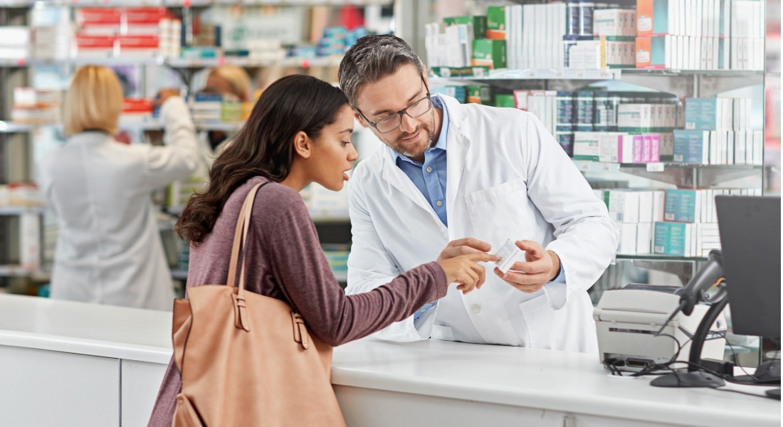 A pharmacist looks at a box of medicine with a customer.