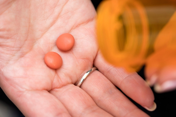 A woman pours two tablets of ibuprofen out of a bottle.