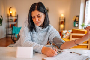 Woman feeling sick at home and looking worried while checking her health using medical devices and writing down results
